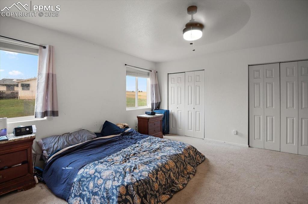 Image 25 of 38: Bedroom with two closets, light carpet, and ceiling fan