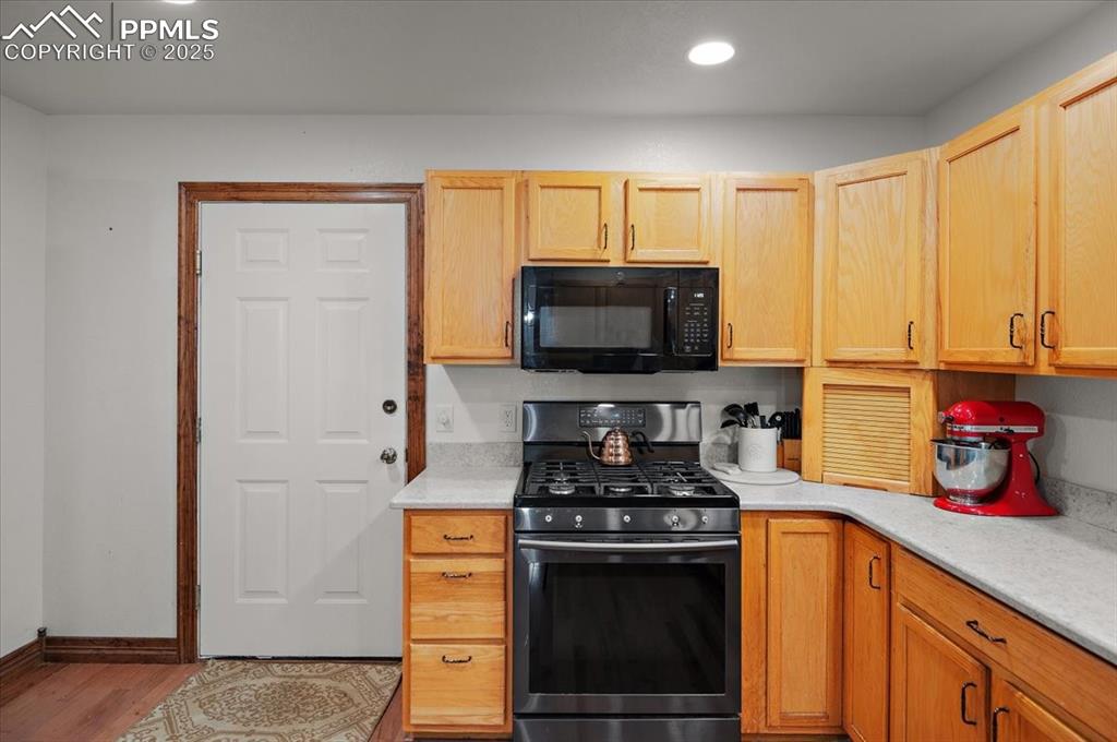 Image 7 of 38: Kitchen with black microwave, stainless steel gas stove, light countertops,