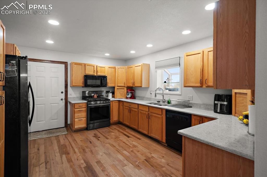 Image 9 of 38: Kitchen with black appliances, a sink, recessed lighting, and light wood fi