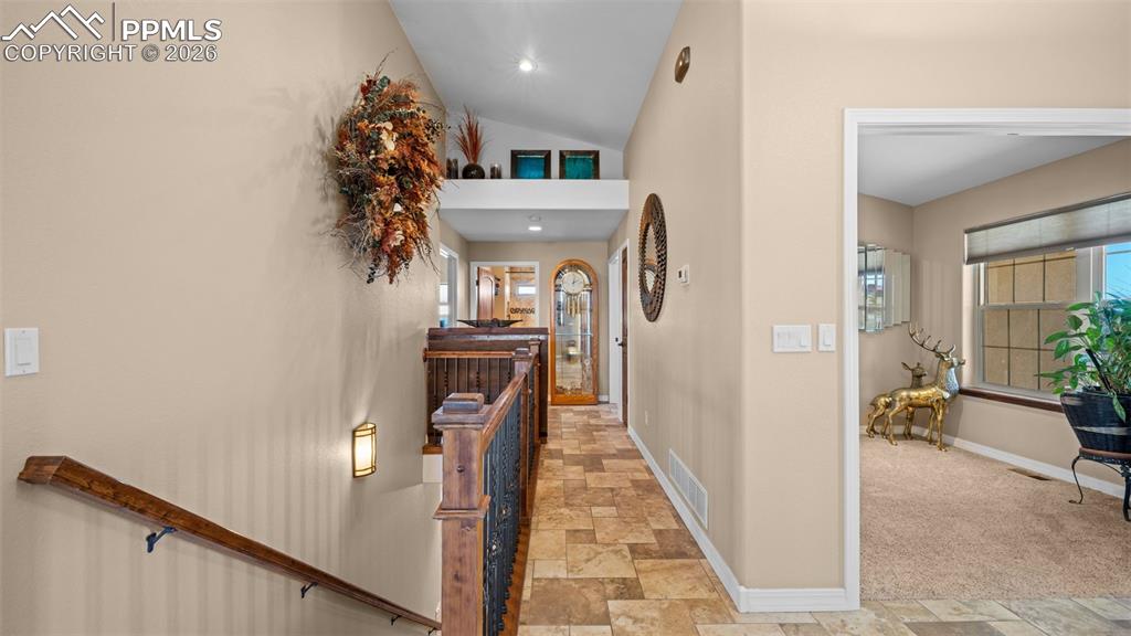 Image 15 of 47: Corridor featuring stone finish floors, lofted ceiling, and an upstairs lan