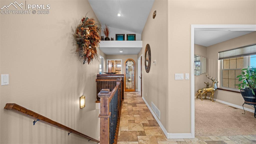Image 16 of 50: Corridor featuring stone finish floors, lofted ceiling, and an upstairs lan