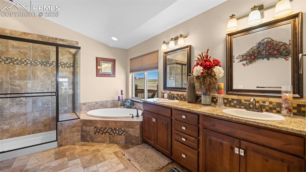 Image 23 of 50: Bathroom with stone tile floors, double vanity, a bath, a stall shower, and