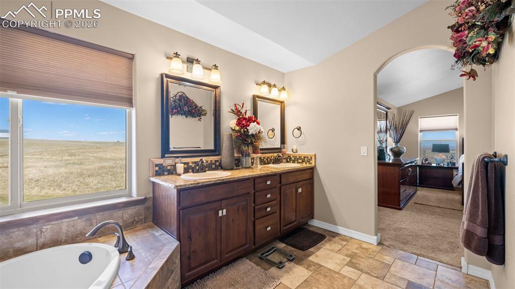 Image 25 of 50: Ensuite bathroom featuring double vanity, a garden tub, light stone finish