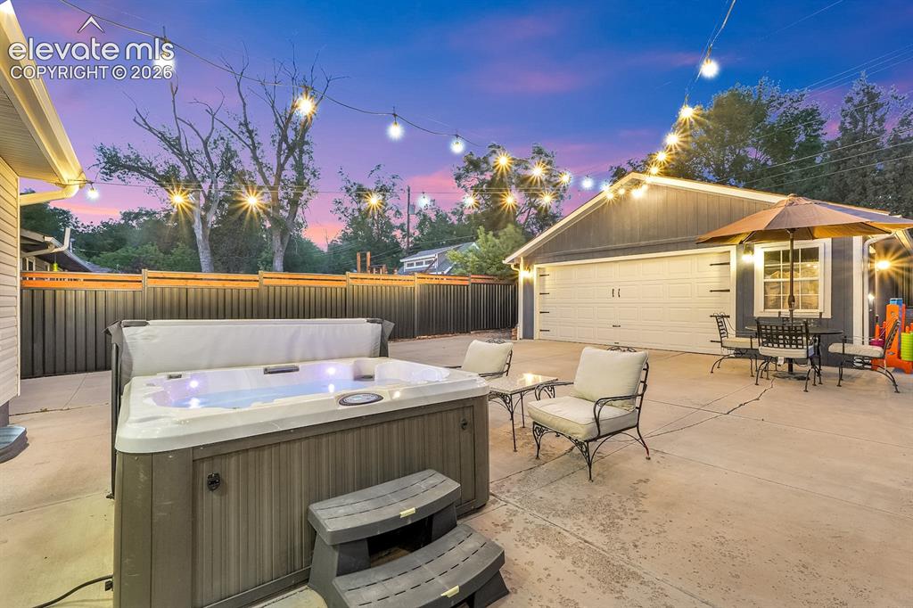 Image 22 of 33: Expansive concrete patio featuring a hot tub with steps, string lighting, a