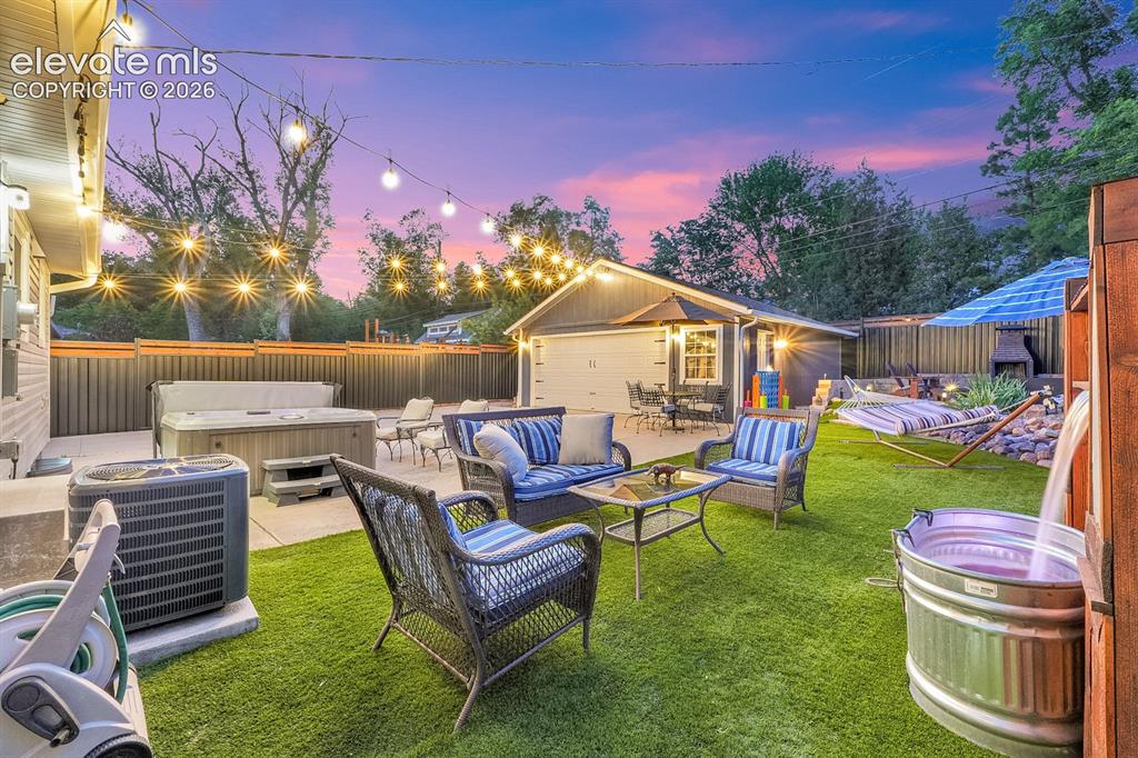 Image 6 of 33: Manicured lawn with a privacy fence, string lighting, and an attached garag