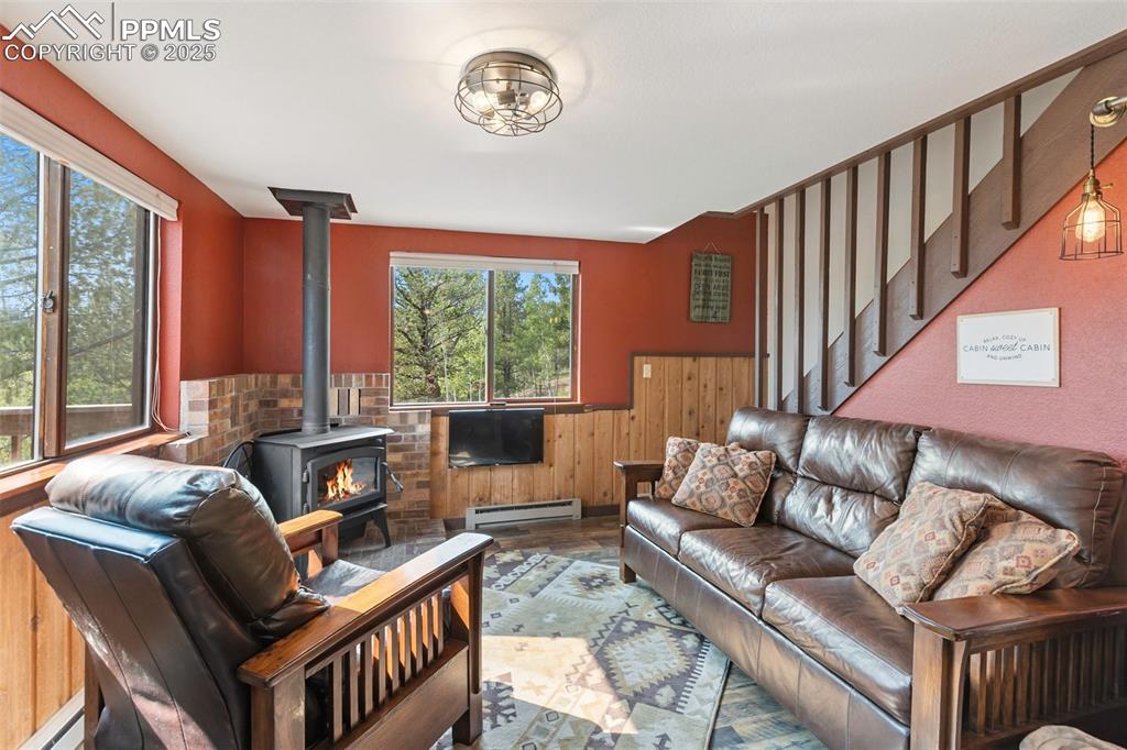 Image 12 of 45: Living room featuring a wainscoted wall, a wood stove, wooden walls, a base