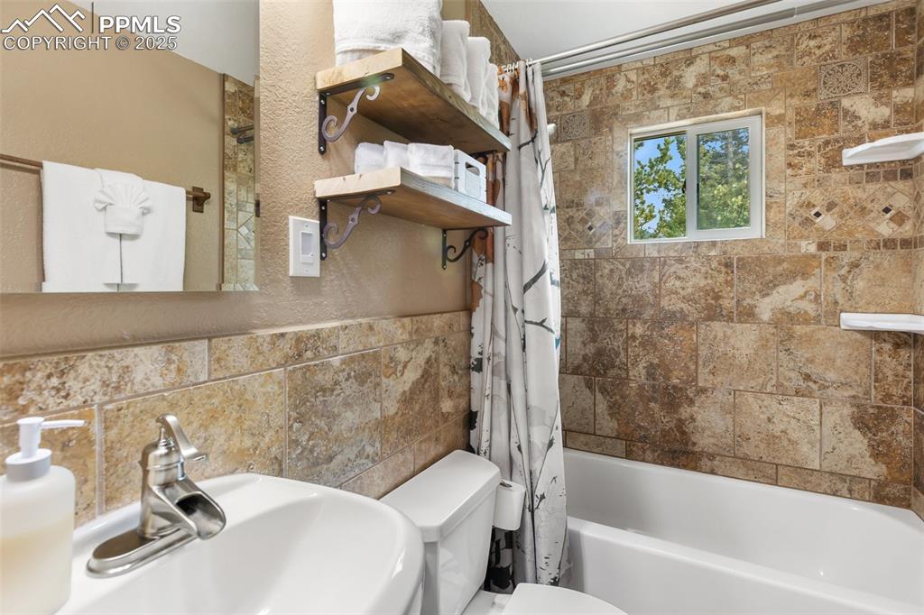 Image 23 of 45: Upper level Bathroom featuring shower / bath combo, tile walls, and a textu