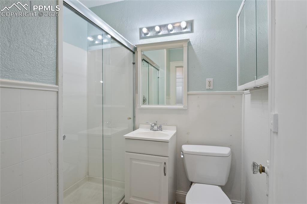 Image 21 of 28: Full bath with a shower, tile walls, and vanity