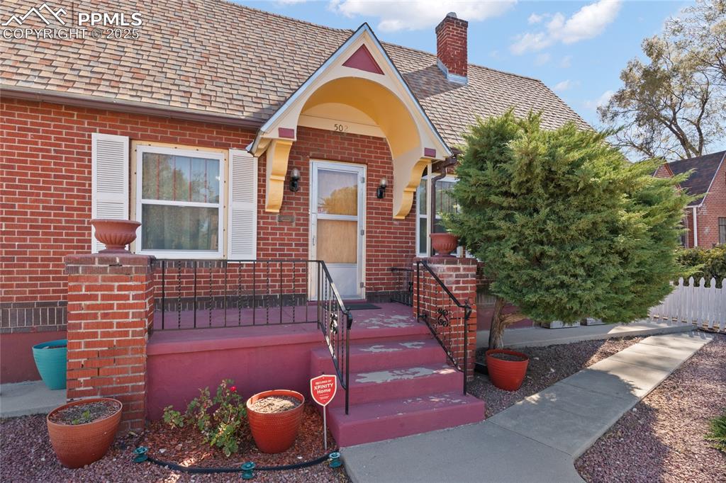 Image 7 of 28: View of front of home with brick siding, a chimney, and roof with shingles
