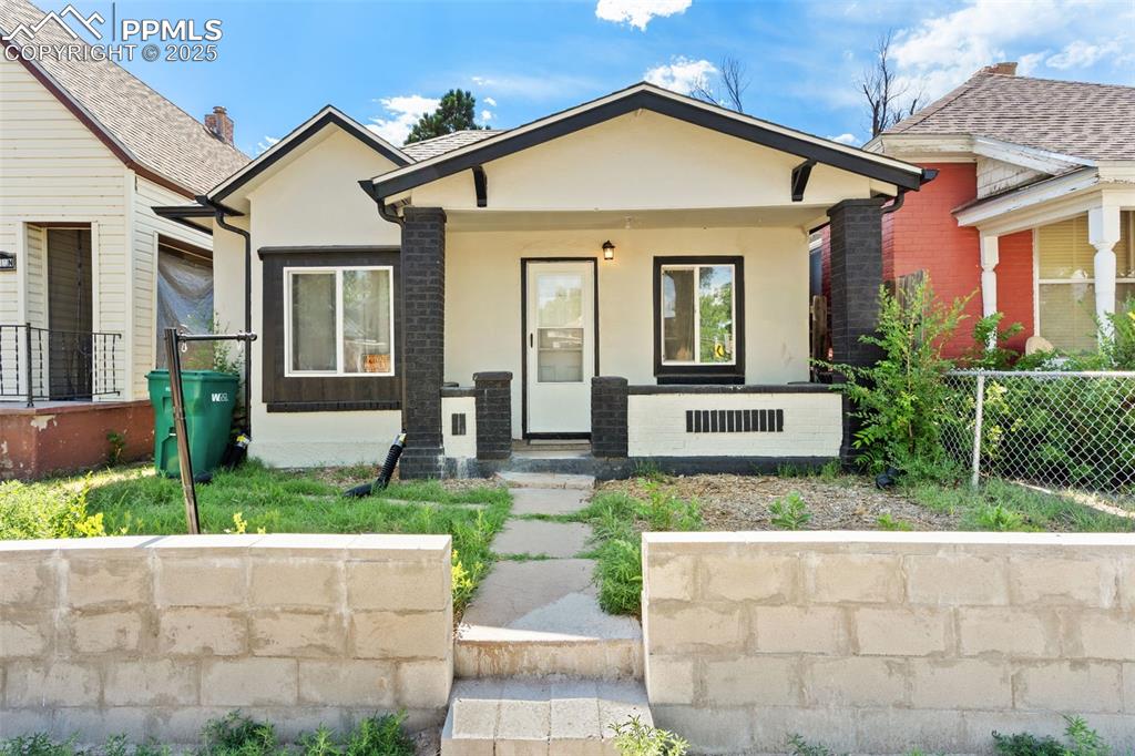 Caption: View of front facade with covered porch and stucco siding