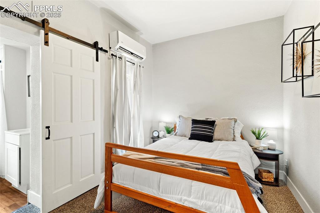 Image 10 of 13: Carpeted bedroom featuring a barn door and a wall unit AC