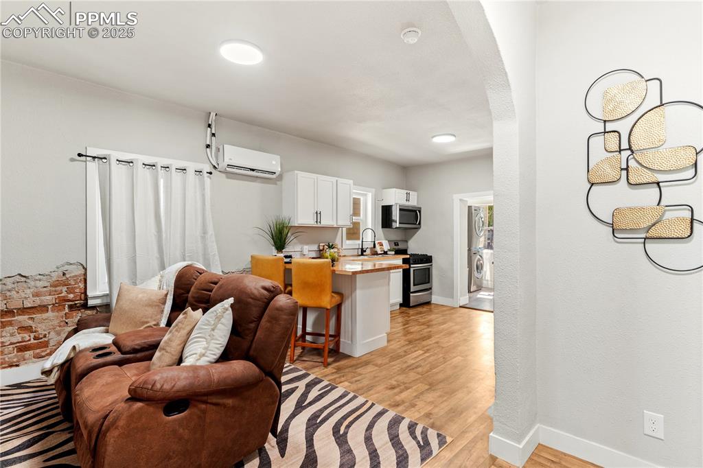 Image 2 of 13: Living area featuring a wall mounted AC, arched walkways, light wood-style 