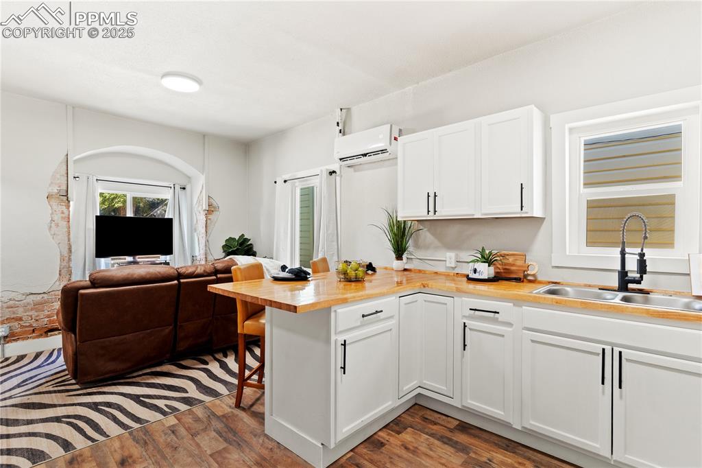 Image 7 of 13: Kitchen with a wall unit AC, a peninsula, wooden counters, white cabinetry,