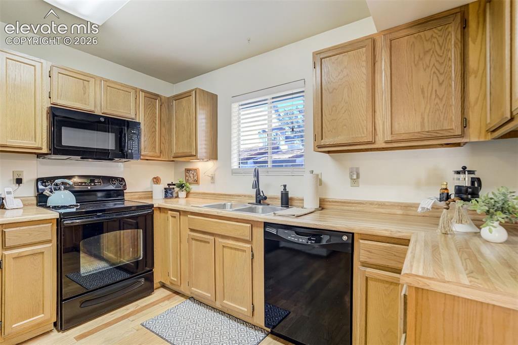 Image 11 of 50: Kitchen featuring light wood-finish cabinetry, black appliance suite, dual 