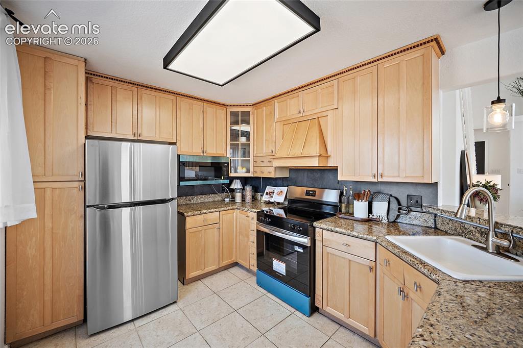 Image 10 of 40: Kitchen featuring wood cabinetry, light-colored tile flooring, stainless st