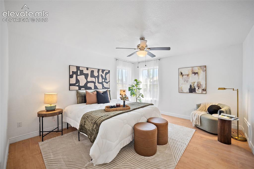 Image 12 of 40: Light-filled bedroom featuring wood-finish flooring, white walls, and a cei