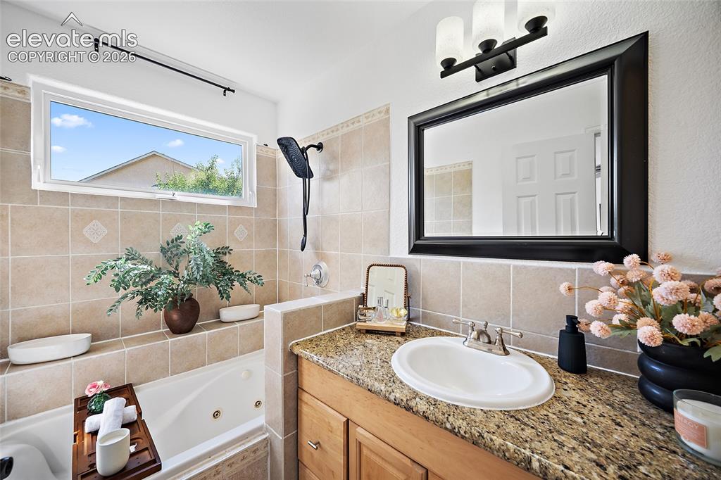 Image 14 of 40: Bathroom featuring a jetted tub, tiled surround with inset detailing, and a
