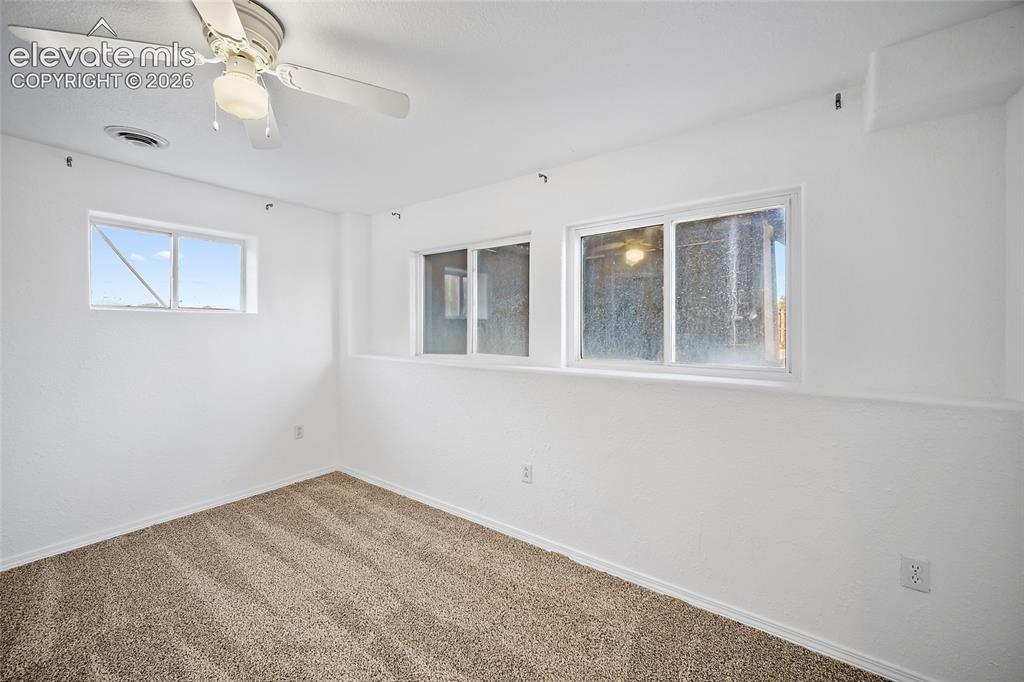 Image 30 of 40: Carpeted room with white walls, multiple windows, a ceiling fan with integr