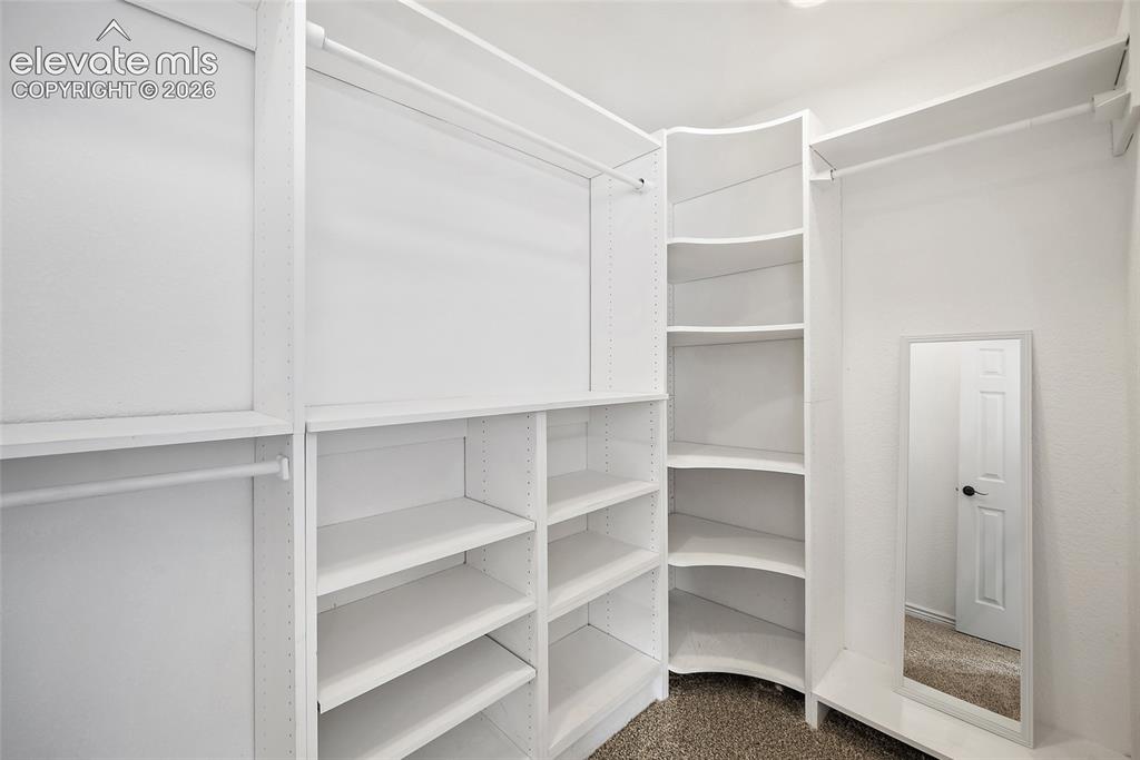 Image 33 of 40: Walk-in closet featuring white built-in shelving, multiple hanging rods, an