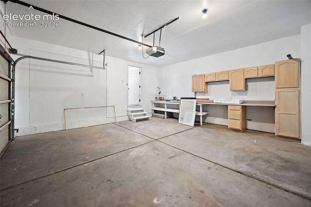 Image 34 of 40: Spacious garage with light-toned cabinetry and integrated workbench