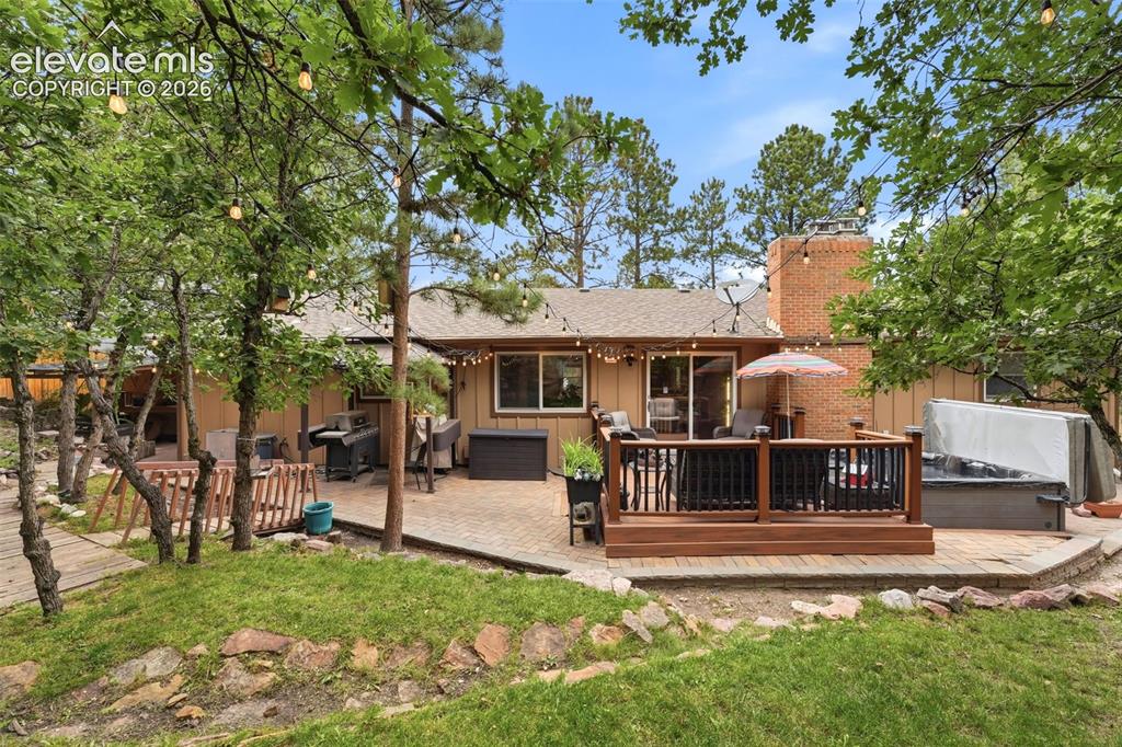 Image 37 of 42: Rear exterior with a wood-tone deck, paved patio, brick chimney, and surrou
