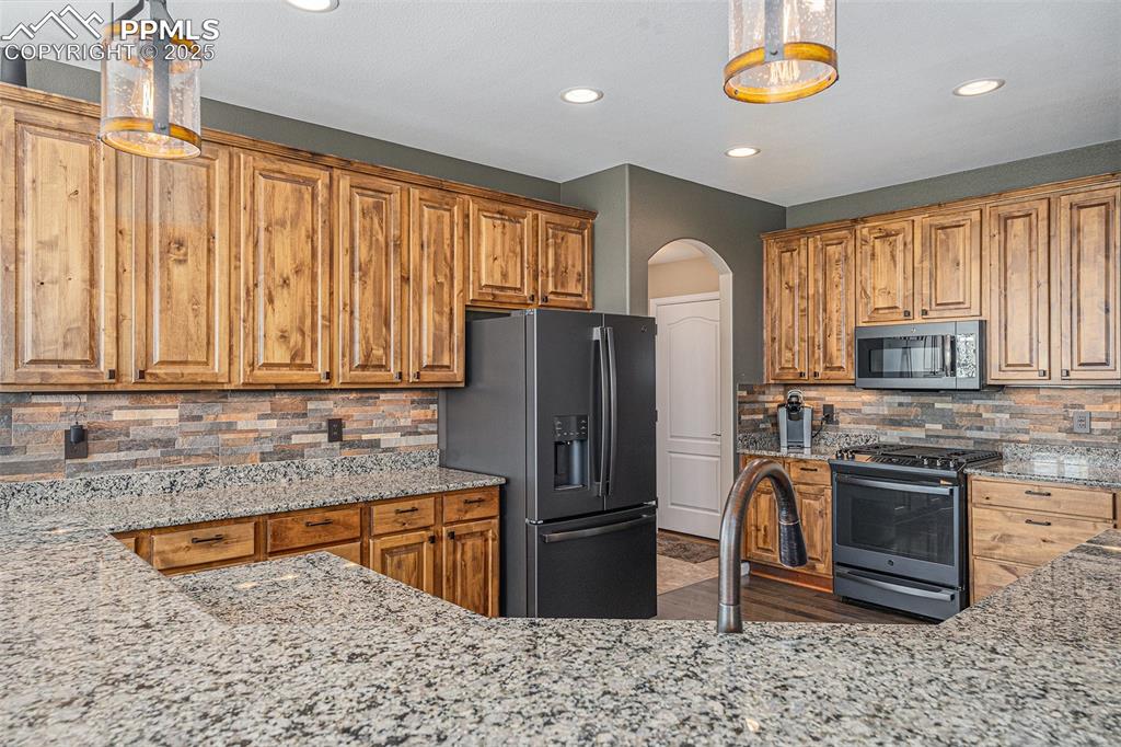 Image 10 of 48: Kitchen featuring light stone countertops, gas stove, refrigerator with ice