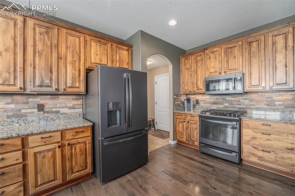 Image 11 of 48: Kitchen with decorative backsplash, arched walkways, appliances with stainl