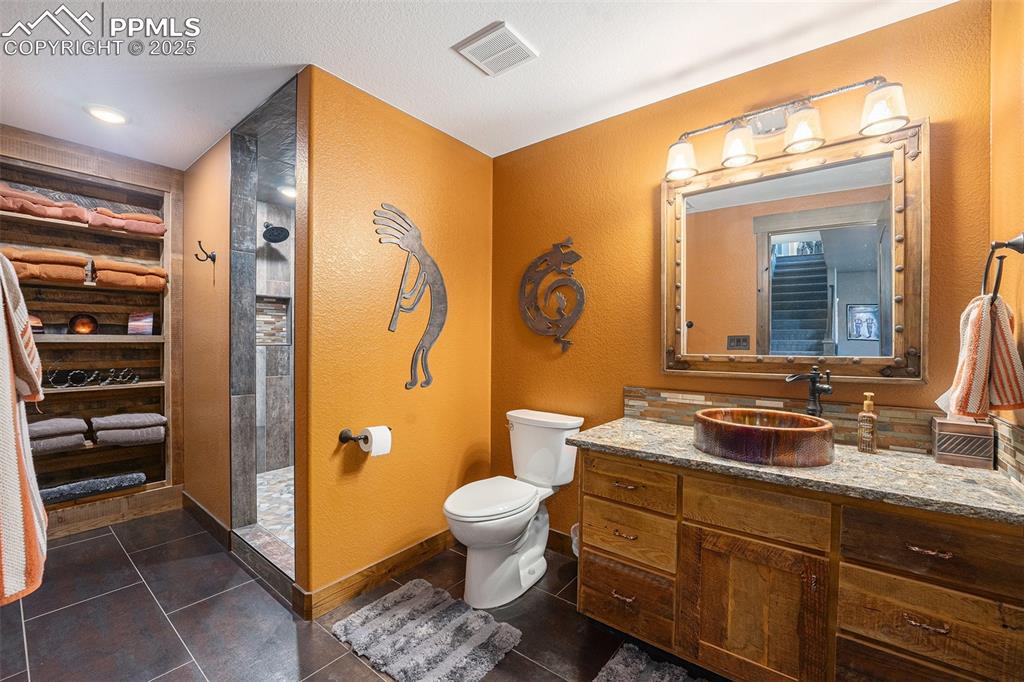 Image 34 of 48: Bathroom with a textured wall, vanity, a walk in shower, and dark tile patt