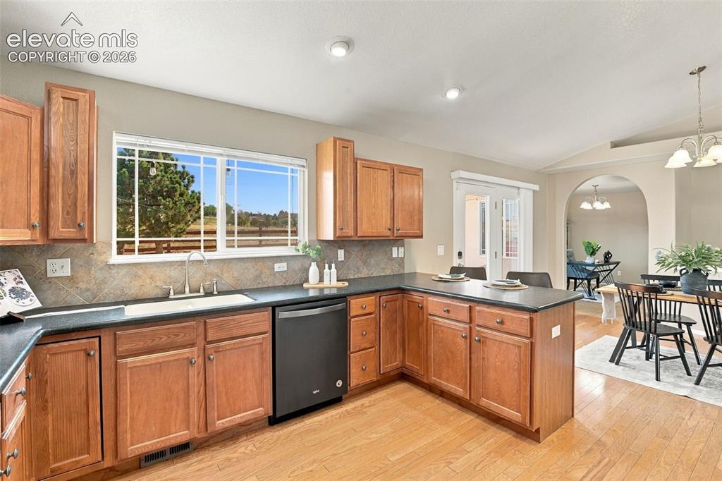 Image 11 of 50: Wood-finish flooring, wood cabinetry, tile backsplash, black countertops, a