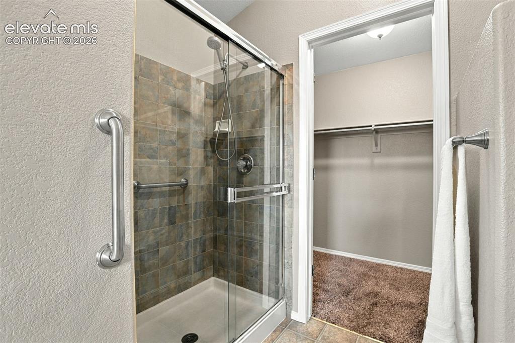 Image 26 of 50: Glass-enclosed shower with tiled surround, handheld shower fixture, and bui