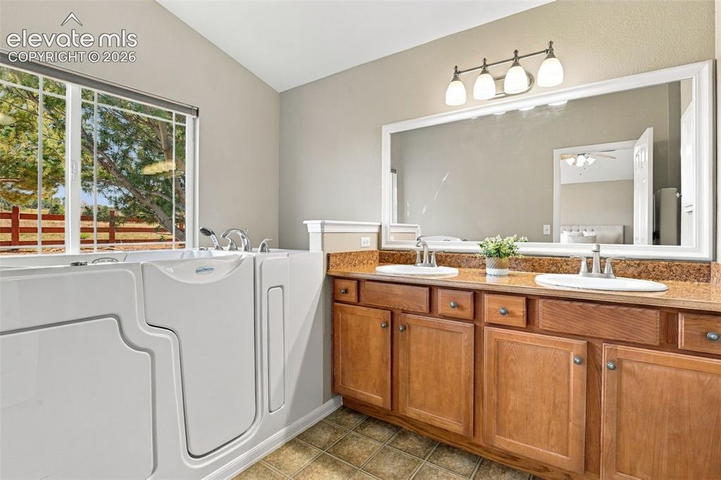 Image 27 of 50: Walk-in tub with window, double vanity with stone-finish countertop, and in