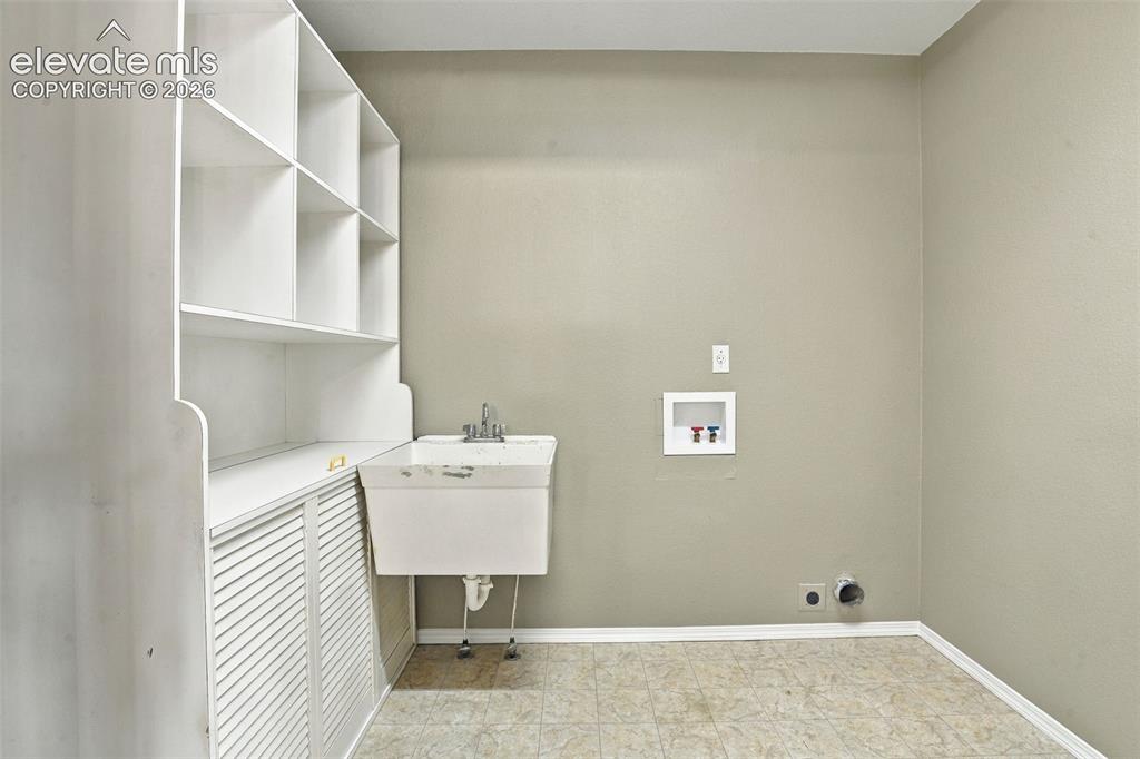 Image 31 of 50: Laundry area with white built-in shelving, white louvered cabinetry, and a