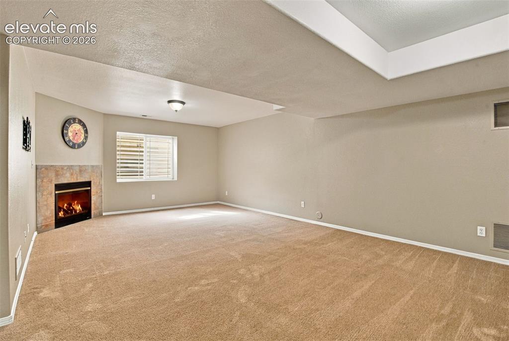 Image 32 of 50: Spacious carpeted room featuring a corner fireplace with a tiled surround, 