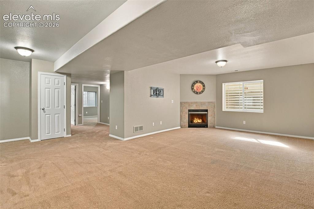 Image 33 of 50: Carpeted room featuring a corner fireplace with a tile surround, a window w