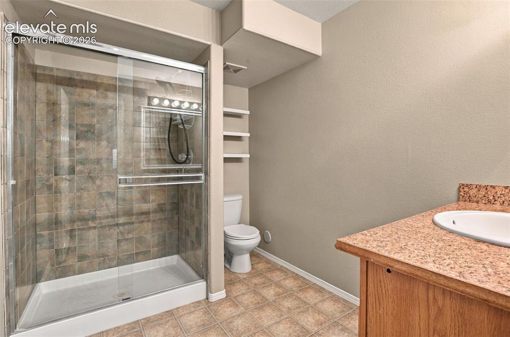Image 37 of 50: Glass-enclosed shower with tile surround, built-in shelving, wood-finish va