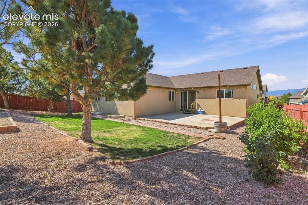 Image 48 of 50: Expansive backyard featuring a concrete patio, mature trees, and a gravel p