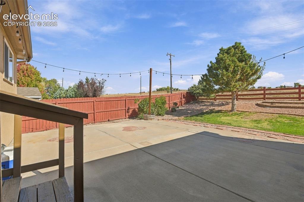 Image 49 of 50: Expansive concrete patio with string lighting, bordered by a wooden privacy