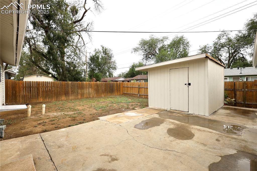 Image 24 of 27: Fenced backyard with a patio and a storage shed