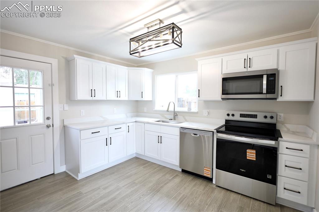 Image 5 of 27: Kitchen featuring stainless steel appliances, white cabinetry, light wood-s