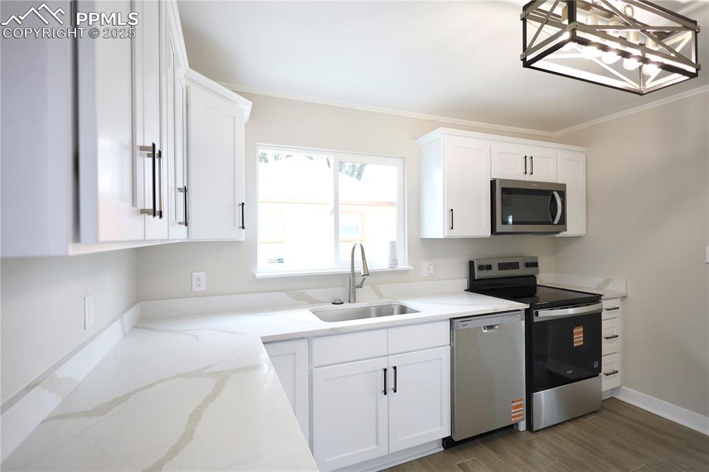 Image 6 of 27: Kitchen with white cabinetry, stainless steel appliances, crown molding, li