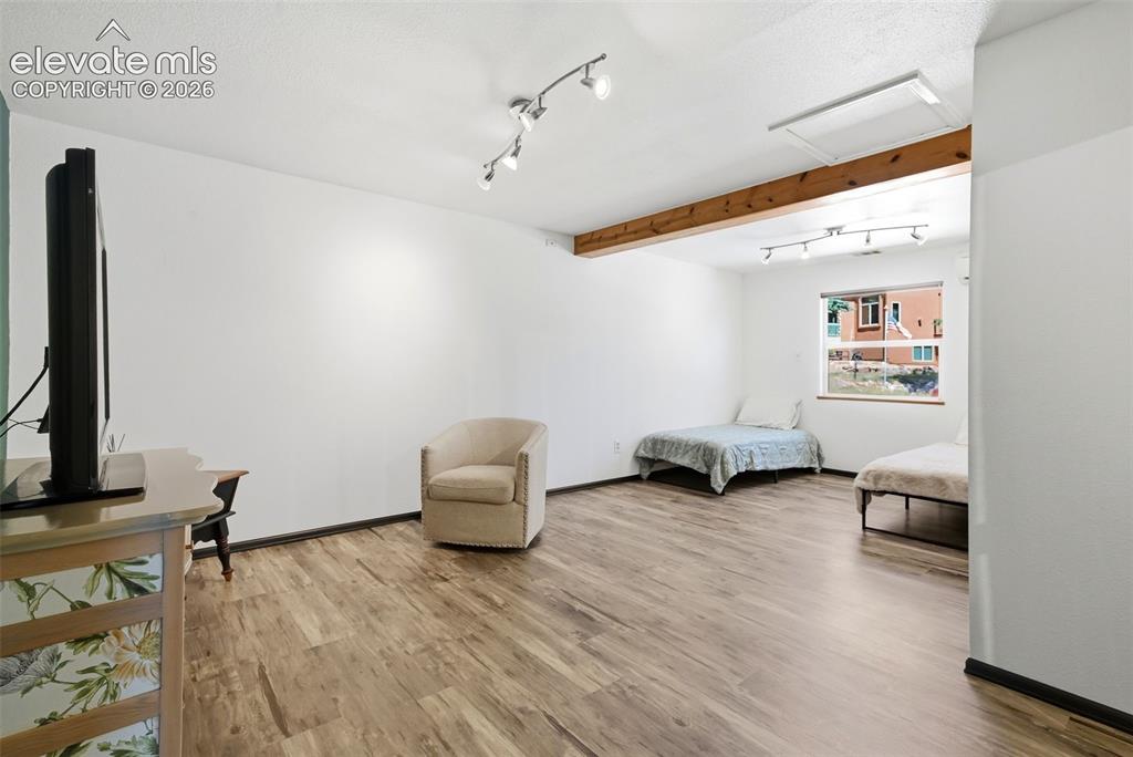 Image 21 of 50: Spacious room featuring wood-finish flooring, white walls, exposed wood bea