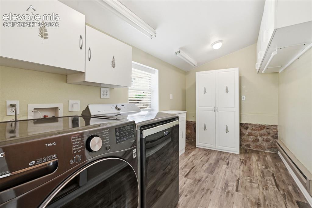 Image 31 of 50: Dedicated laundry area featuring wood-finish flooring, white cabinetry, and