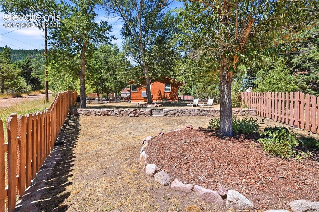 Image 34 of 50: Fenced outdoor area featuring a wood picket fence, a mulched tree ring with