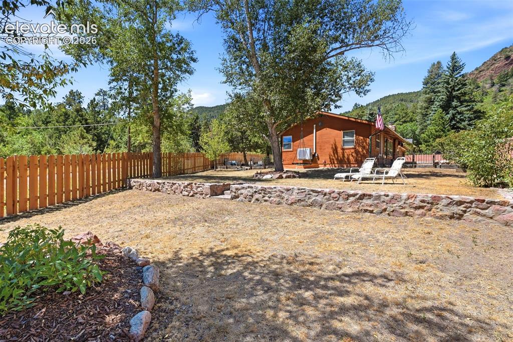 Image 35 of 50: Expansive outdoor area featuring a wood fence, stone retaining wall, and ma