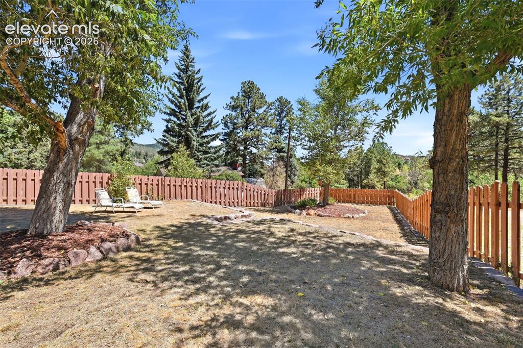 Image 36 of 50: Fenced backyard featuring mature trees, a sloped terrain, and a natural lan