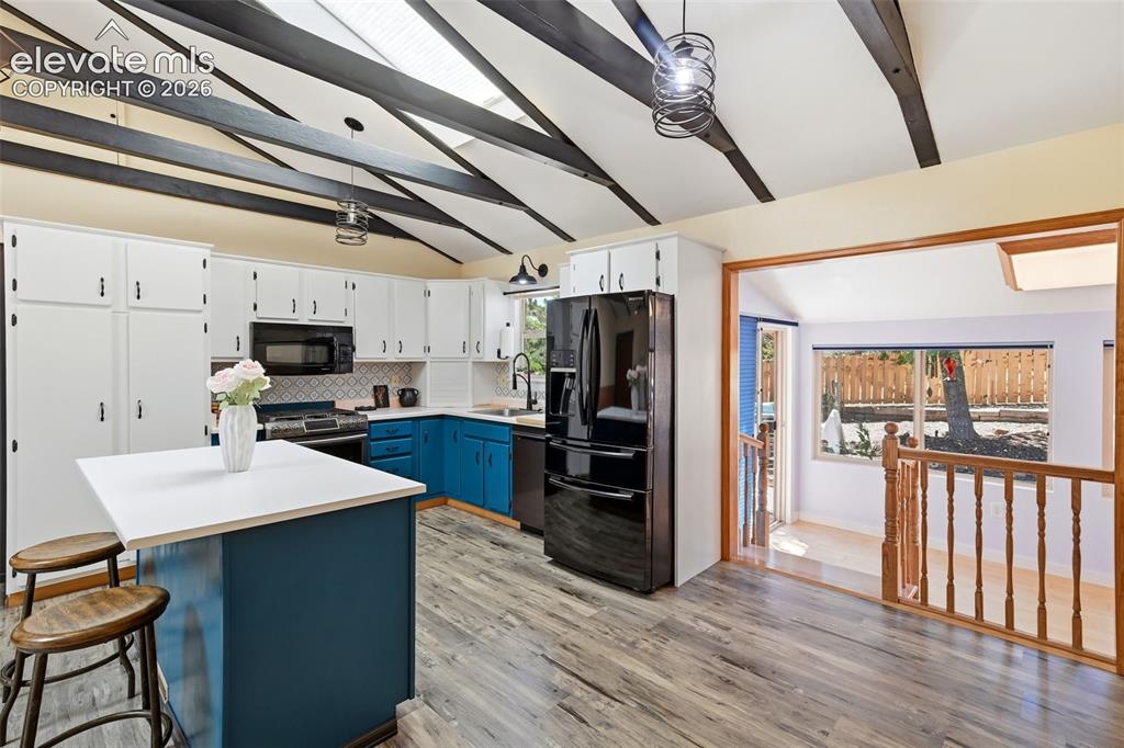 Image 5 of 50: Kitchen featuring vaulted ceilings with exposed beams, white upper cabinetr