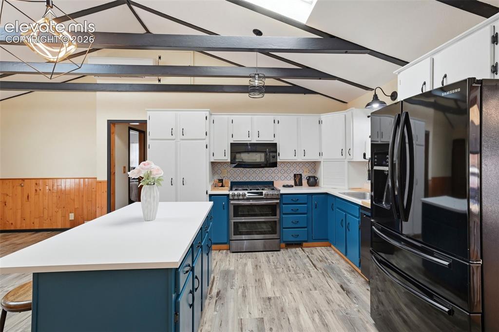 Image 6 of 50: Kitchen featuring a central island with white countertop, blue lower cabine