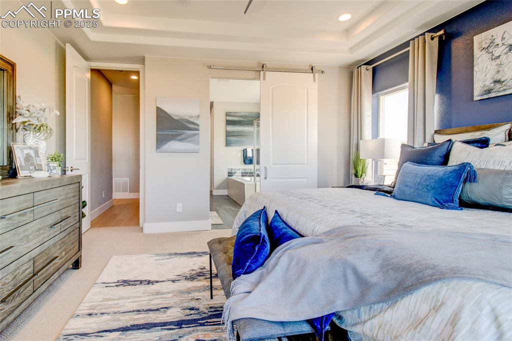 Image 15 of 30: Bedroom featuring a tray ceiling, a barn door, recessed lighting, ensuite b