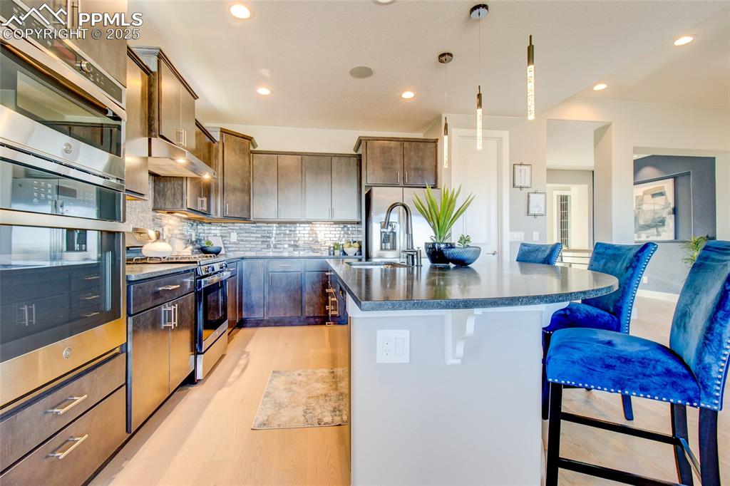 Image 7 of 30: Kitchen with appliances with stainless steel finishes, a kitchen bar, dark