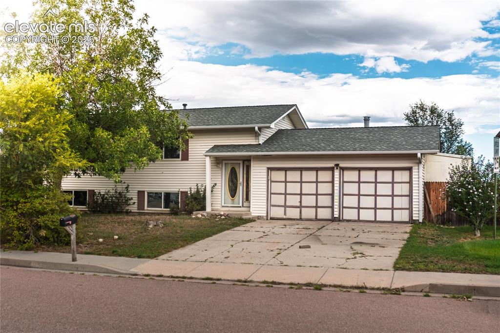 Caption: Two-car garage with panel-style doors, siding exterior, and mature front yard landscaping